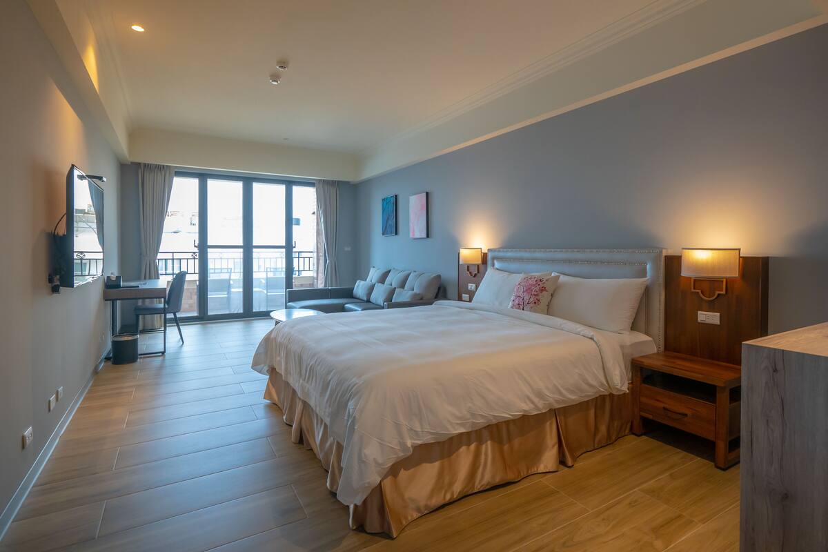 A hotel room with a large bed, a desk, and a balcony with a view.