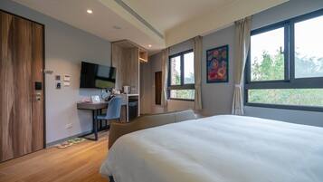 A modern hotel room with a large bed, a desk with a chair, a television, and a window with a view of trees.