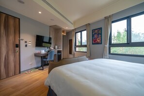 A modern hotel room with a large bed, a desk with a chair, a television, and a window with a view of trees. - Relaxury Beach House (Hengchun)