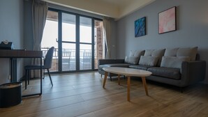 A modern living room with a grey sofa, a round coffee table, and a view through a large sliding glass door to the outside. - Relaxury Beach House (Hengchun)
