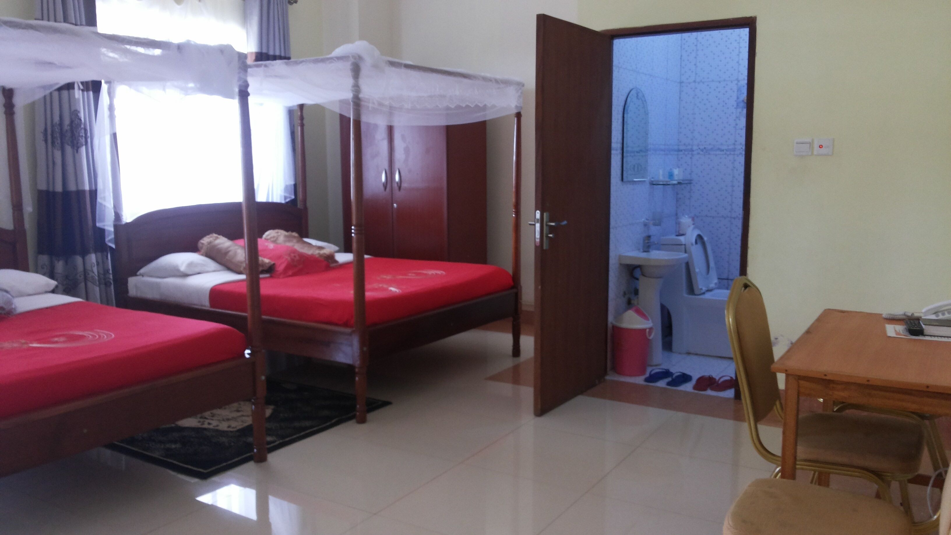 A room with two beds, a wooden table, a chair, and a bathroom visible through an open door.