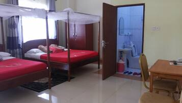 A room with two beds, a wooden table, a chair, and a bathroom visible through an open door.