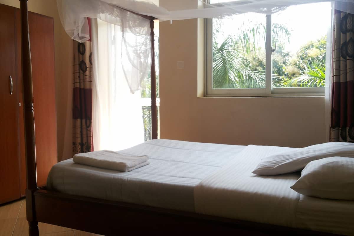 A bedroom with a bed, curtains, a window, and a wardrobe.