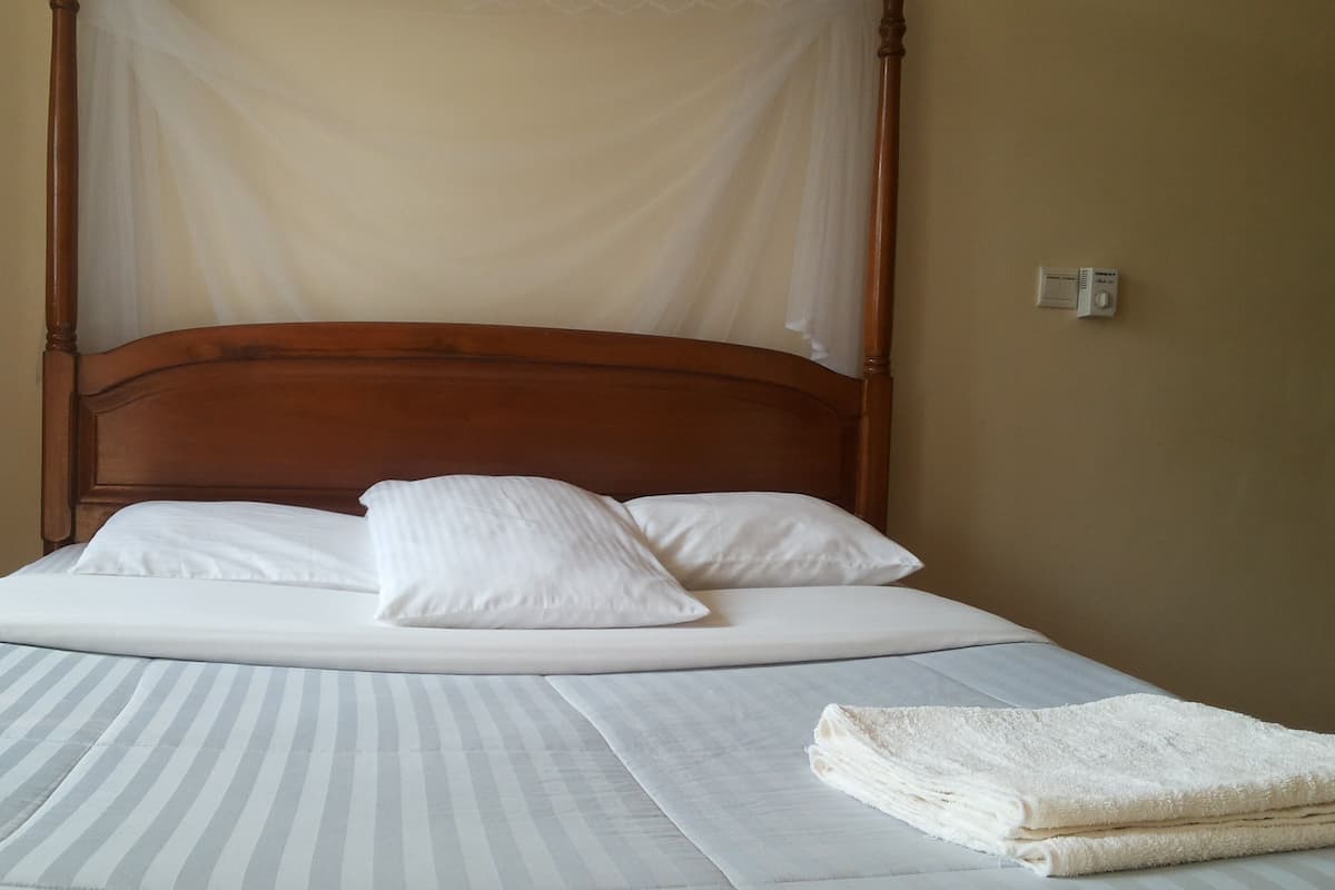 A bed with a canopy, white bedding, and a folded towel on the side.