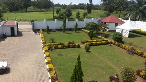 A courtyard with a paved walkway, neatly trimmed hedges, and a white building with a red roof. - Rosevilla Hotel (Arua)