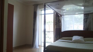 A bedroom with a bed, a window with curtains, and a view of greenery outside. - Rosevilla Hotel (Arua)