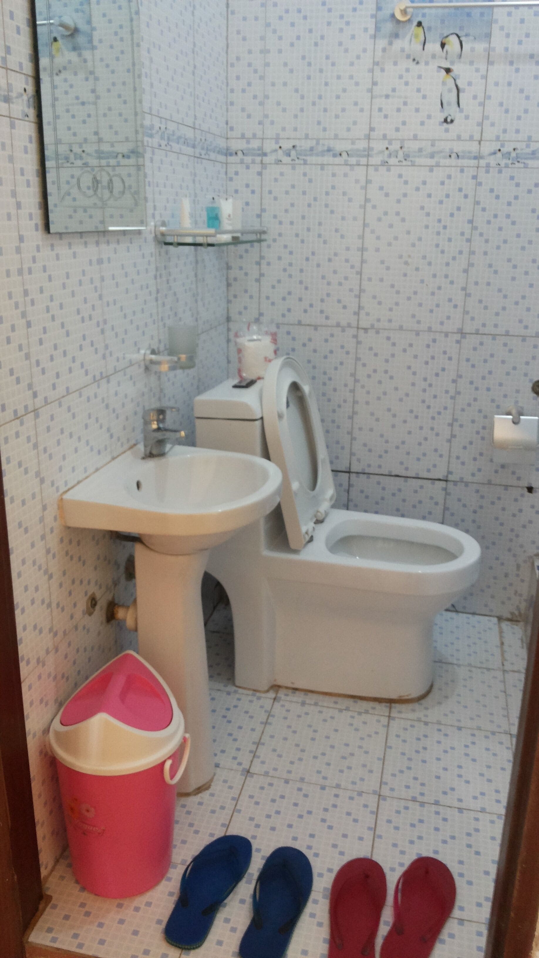 Un baño con inodoro, lavabo y un cubo rosa.