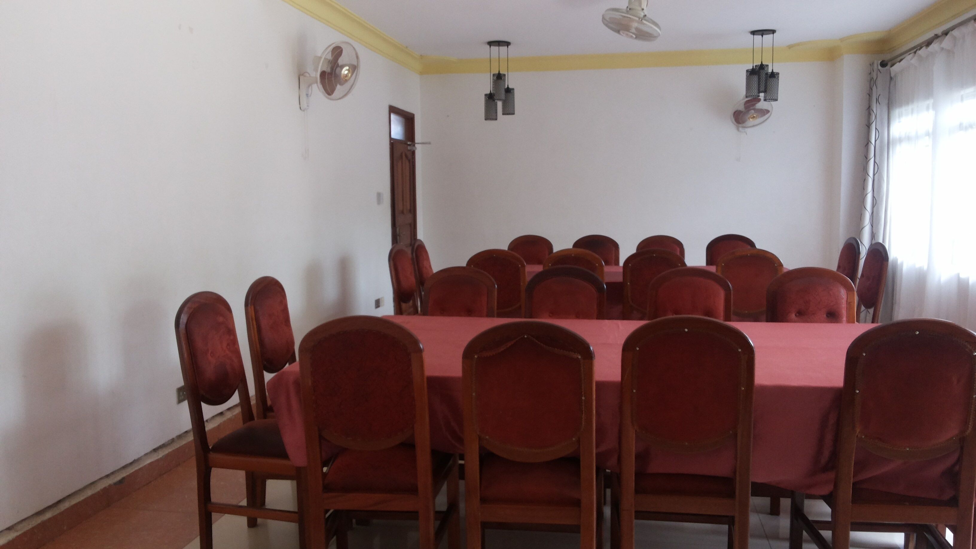 Uma sala de conferência com uma mesa comprida e várias cadeiras, um ventilador de teto e uma janela com cortinas.