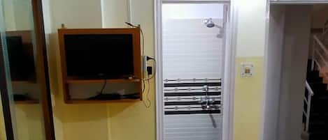 Habitación de hotel con cama, televisor, puerta que da a un baño y un espejo.
