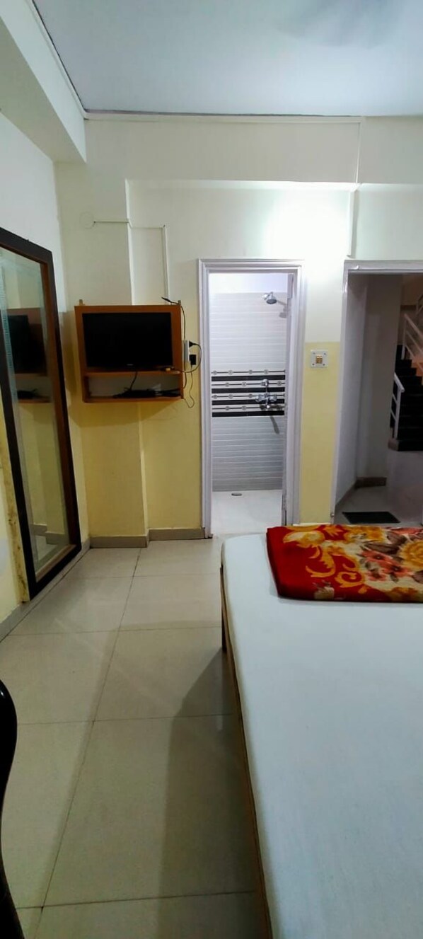 A hotel room with a bed, a television, a door leading to a bathroom, and a mirror.