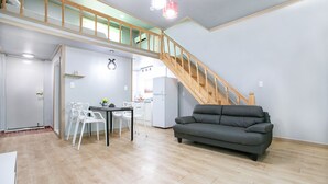 A spacious living area with a wooden staircase, a dining table with chairs, and a grey sofa. - Il Mare Pension (Yangyang)