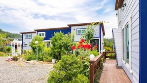 A two-story blue house with a wooden deck and a garden with red flowers. - Il Mare Pension (Yangyang)