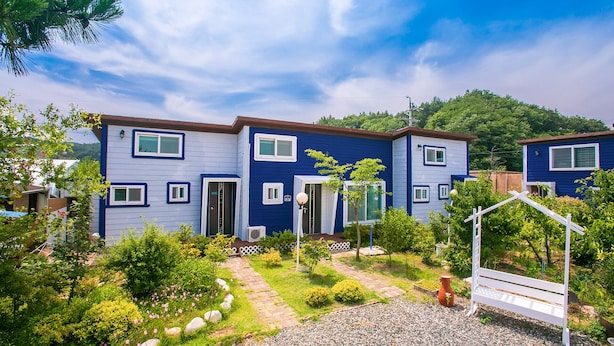 A two-story residential building with a blue exterior, a front garden with a pathway, and a white fence. - Il Mare Pension (Yangyang)