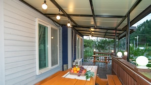 An outdoor covered patio with wooden benches and a picnic table, featuring a basket of fruit and a bottle of water. - Il Mare Pension (Yangyang)