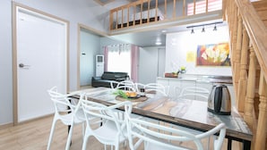 A dining area with a wooden table and white chairs, a kitchenette with a stove and sink, and a staircase leading to an upper level. - Il Mare Pension (Yangyang)