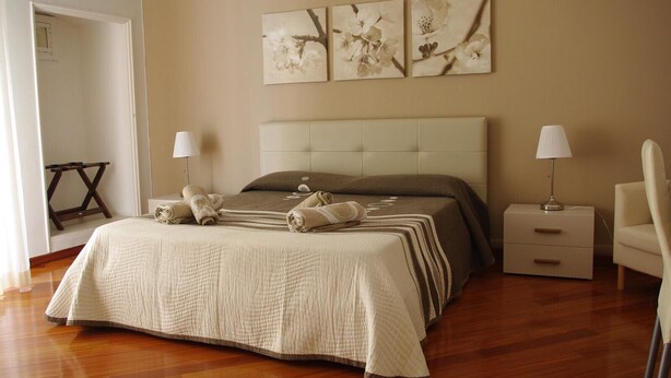 A bedroom with a large bed, two bedside tables, a chair, and wall art. - La Cattedrale B&B (Ruvo di Puglia)