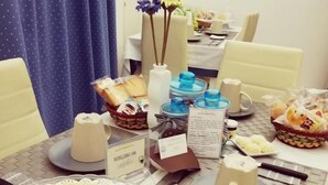A dining table set with various food items, including a cake with heart-shaped cookies, a basket of bread, and a plate of green fruits. - La Cattedrale B&B (Ruvo di Puglia)