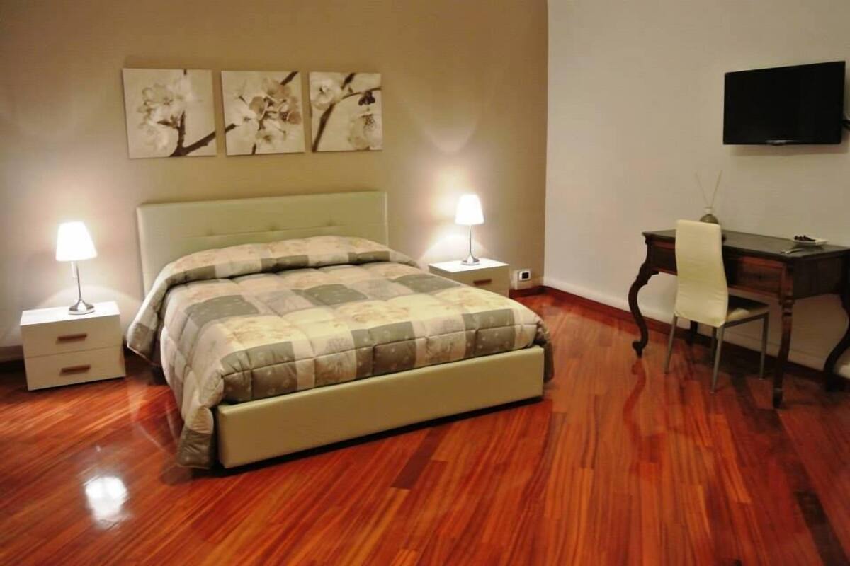 Een slaapkamer met een bed, nachtkastjes, een bureau, een stoel en kunstwerken aan de muur.