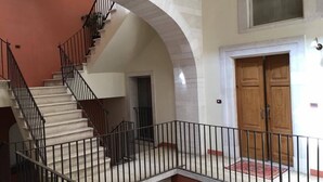 A multi-level interior with a staircase, a wooden door, and a balcony with a metal railing. - La Cattedrale B&B (Ruvo di Puglia)