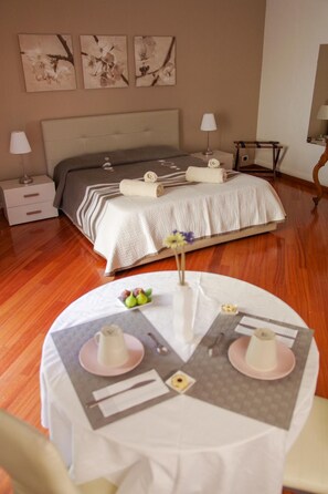 A hotel room with a bed, bedside tables, a round dining table with a white tablecloth, and a vase with flowers.