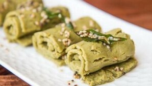 Une assiette blanche contenant des raviolis verts enroulés, décorés de graines de sésame.