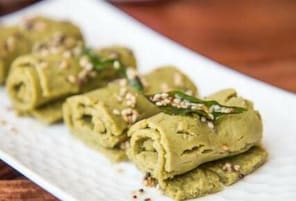 A white plate with rolled green dumplings garnished with sesame seeds.