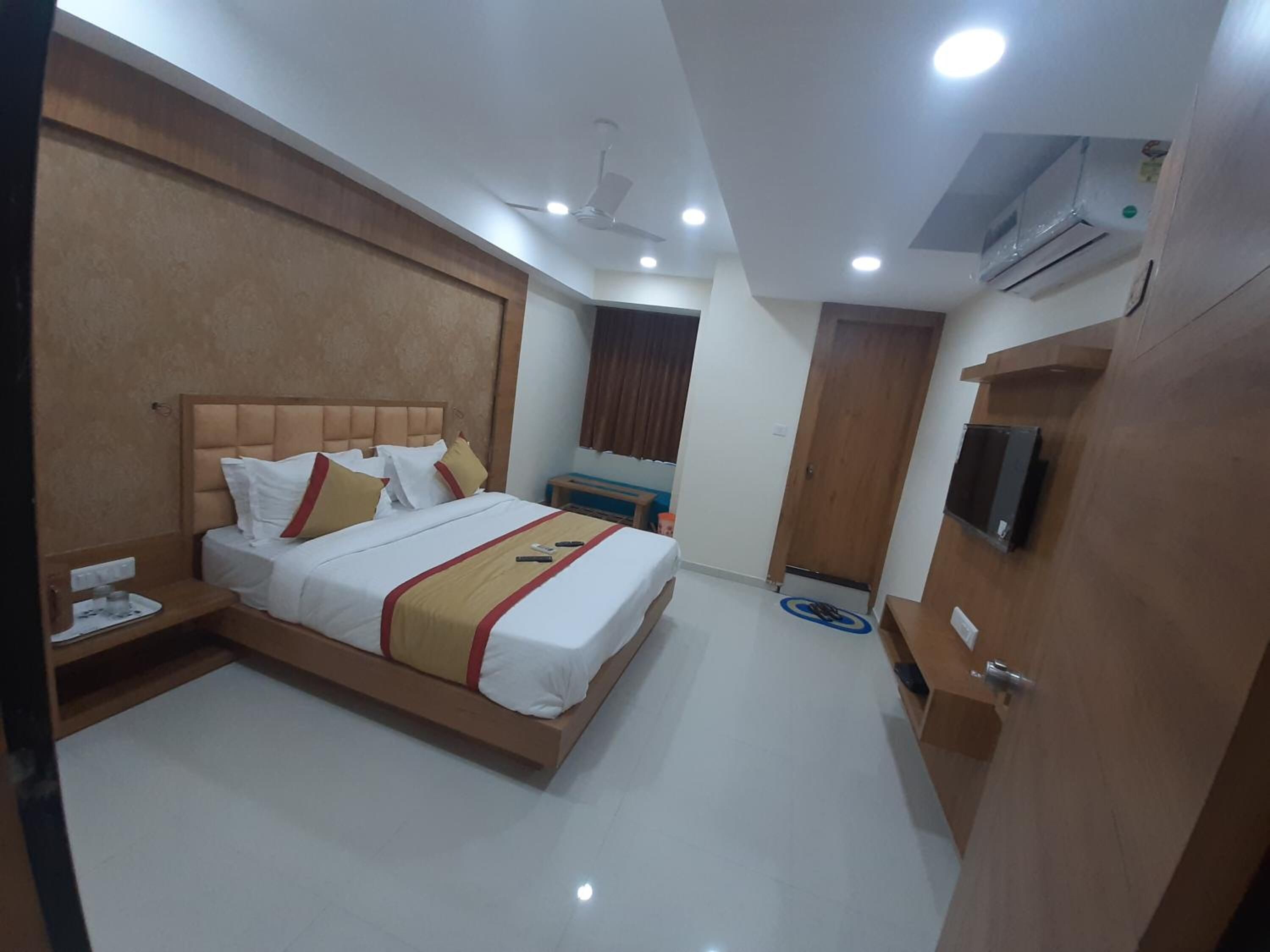 A hotel room with a large bed, bedside tables, a TV, and an air conditioning unit.