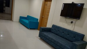 Une pièce avec un canapé bleu, un téléviseur fixé au mur et une porte en bois.