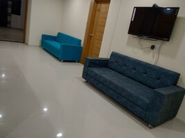 A room with a blue sofa, a television mounted on the wall, and a wooden door.