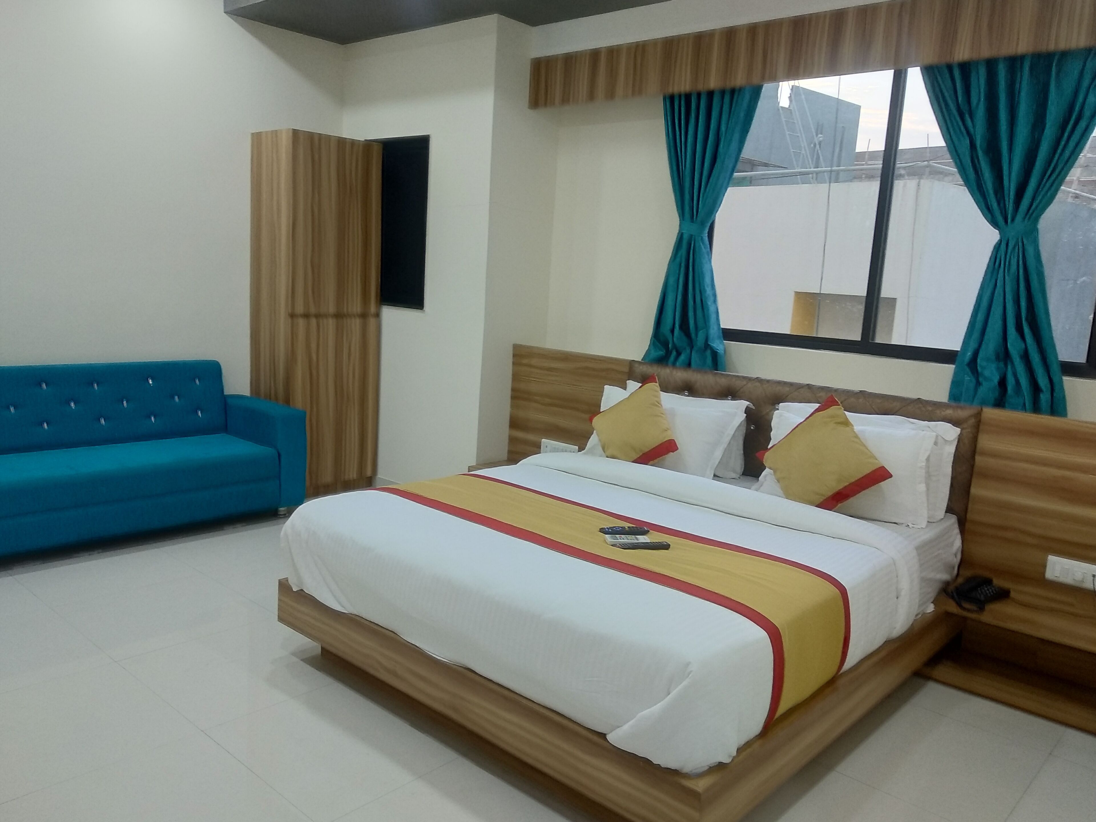 A hotel room with a bed, a blue sofa, and a window with curtains.