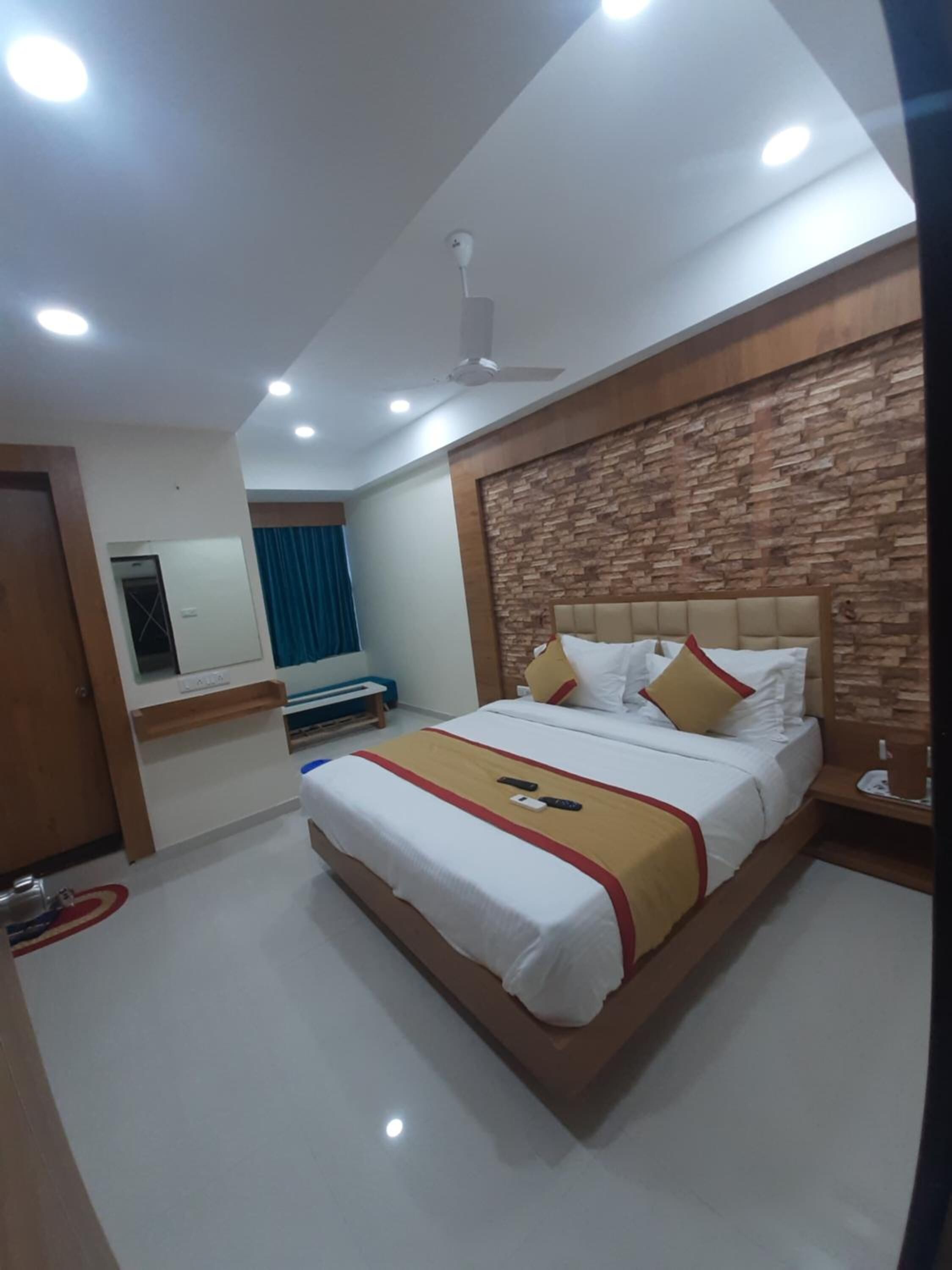 A hotel room with a large bed, a wooden headboard, a flat-screen TV, and a ceiling fan.