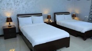 A hotel room with two single beds, each with a nightstand and a lamp. The room has a tiled floor and a textured wall. - Lalibela Roha Tour (Lalibela)