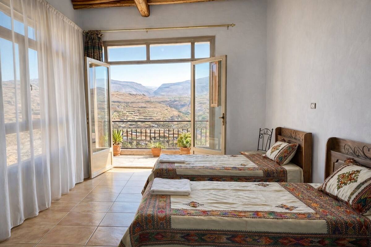A bedroom with two beds, a balcony with potted plants, and a view of a mountainous landscape.