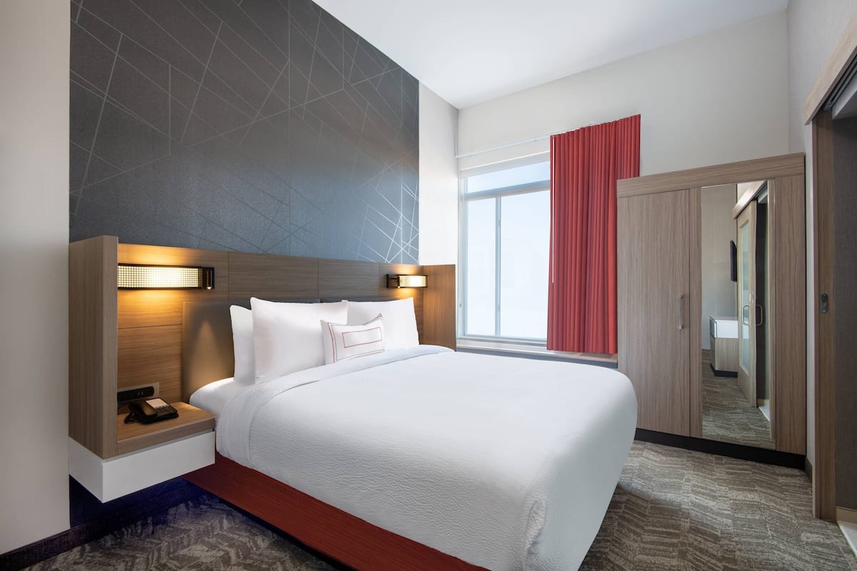 Quarto de hotel com uma cama grande, mesas de cabeceira, um espelho e um guarda-roupa.
