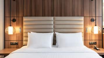 Habitación de hotel con cabecera de madera, dos lámparas de noche, una cama con ropa blanca y una mesita de noche con un teléfono.