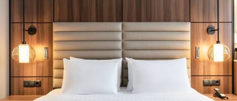 A hotel room with a wooden headboard, two bedside lamps, a bed with white linens, and a nightstand with a phone.