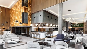 Un espace lounge moderne doté de sièges, d’un bar et d’un plafond haut orné de motifs géométriques sur les murs.