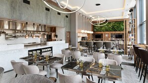 Un restaurant moderne avec des tables surmontées de marbre, des chaises rembourrées et un bar central.