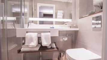 Un bany modern amb dutxa de vidre, vàter blanc i un lavabo amb mirall.