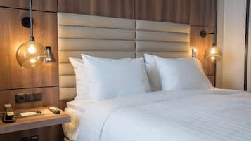 Una cama con ropa de cama blanca, cabecera de madera y lámparas de noche.