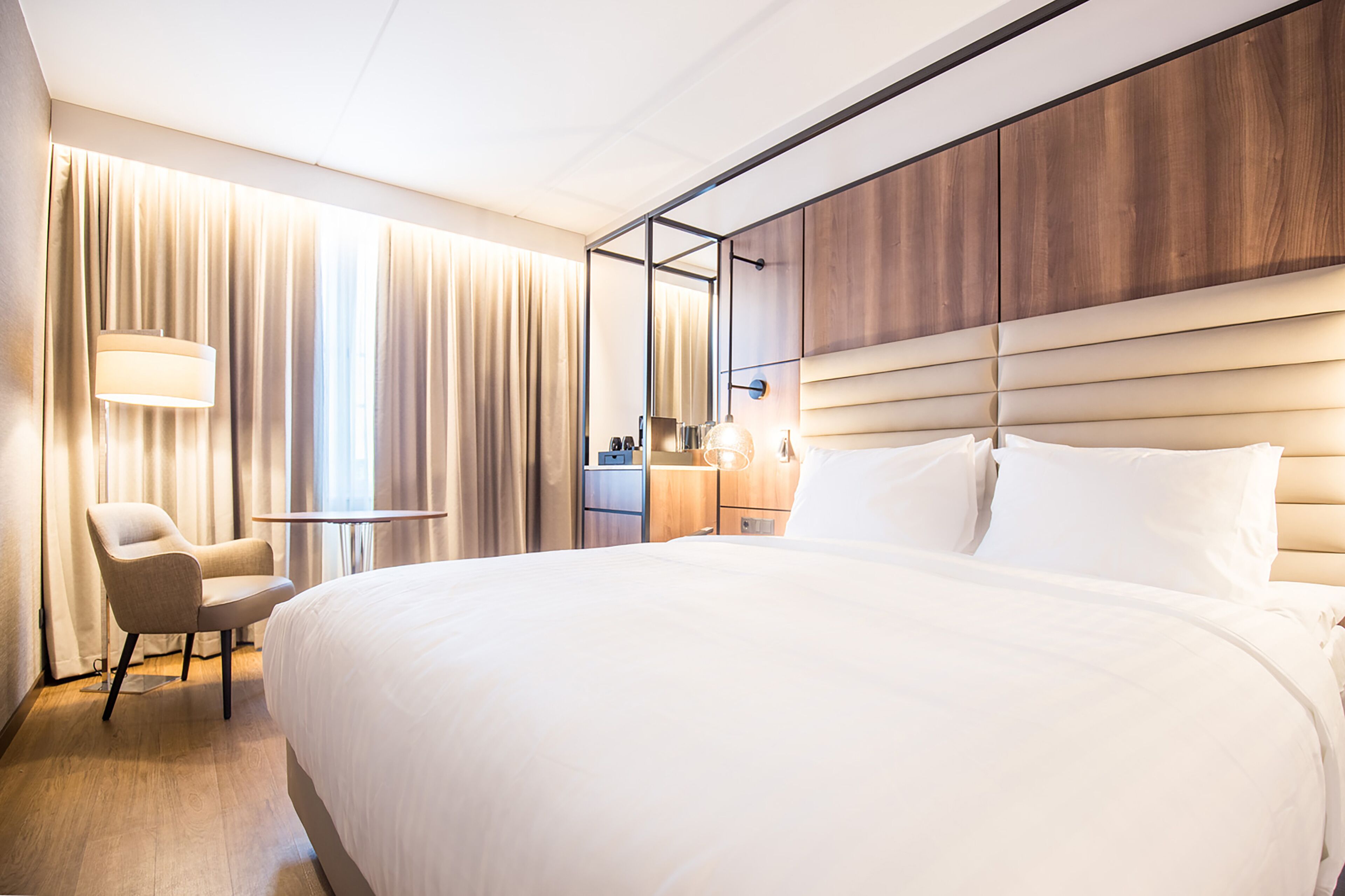 Una camera d'albergo moderna con un letto grande, un comodino, una sedia e uno specchio.