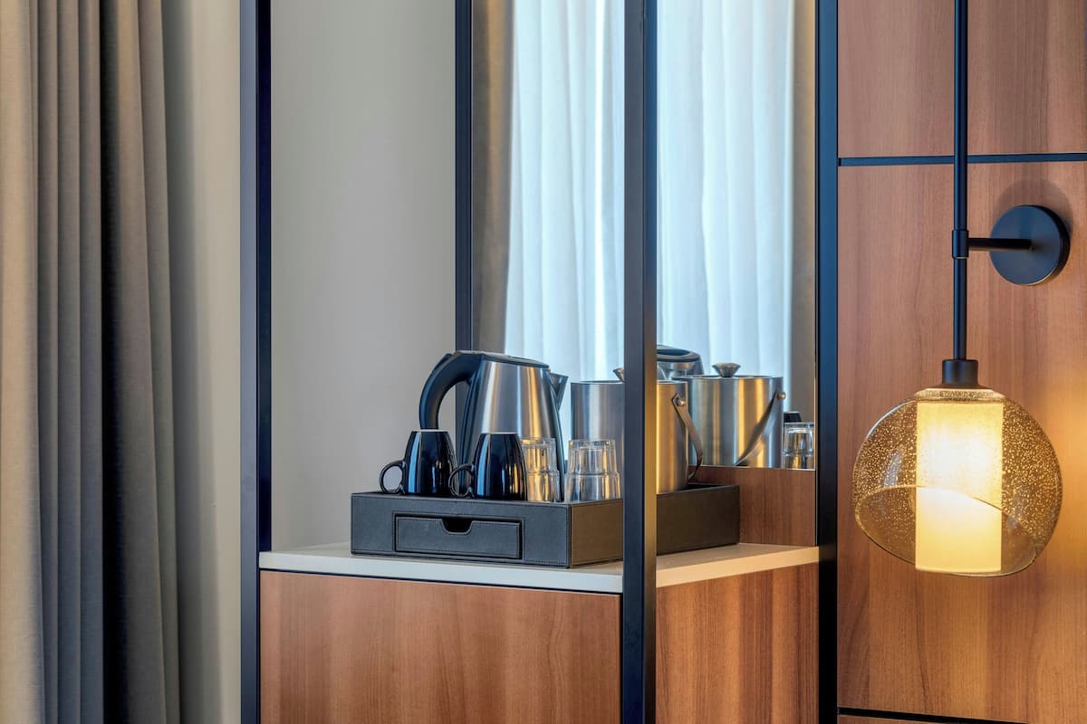 A modern hotel room with a wooden cabinet, a mirror, and a tray with kitchen items.