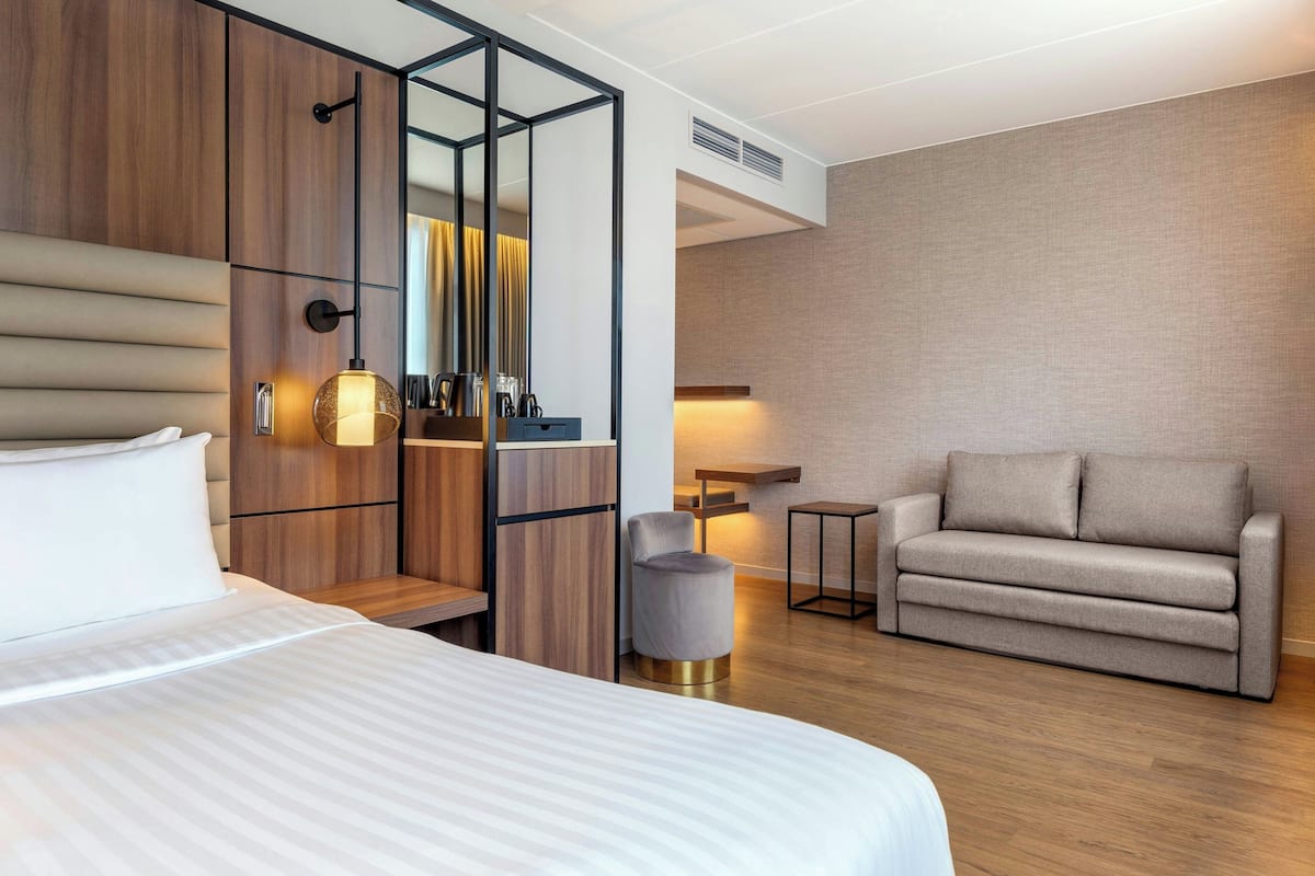 A modern hotel room with a large bed, a sofa, a small table, and a mirror.