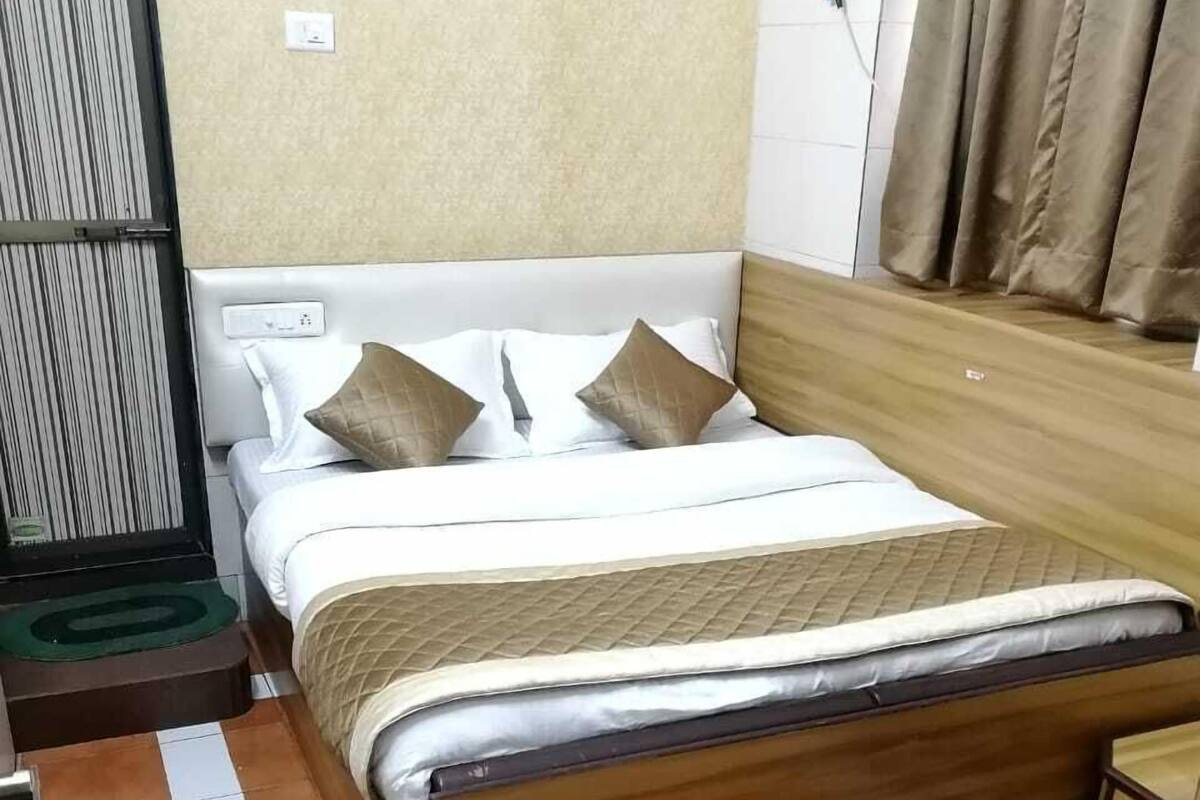 A neatly made bed with a wooden frame and white bedding, a small bedside table, and a wall-mounted power outlet.