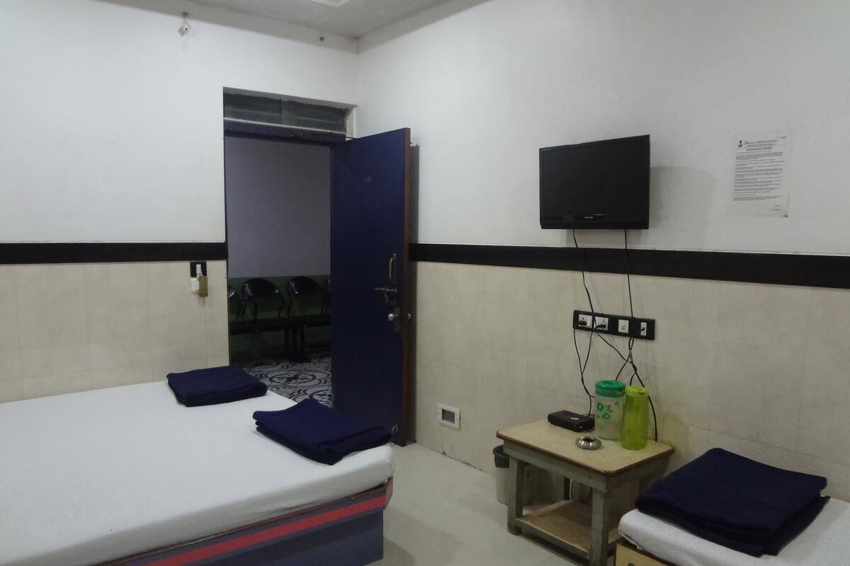A single-bed room with a desk, a chair, a television mounted on the wall, and a small window.