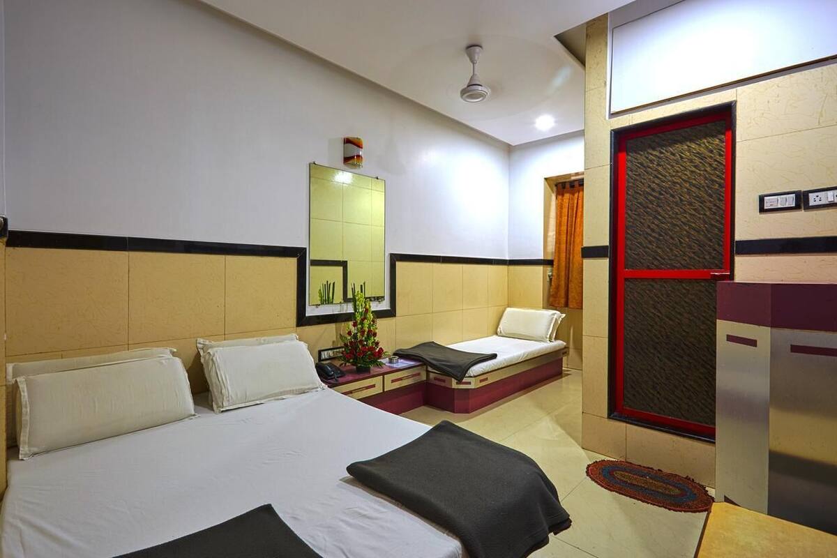 A hotel room with two beds, a small sofa, a mirror, and a red-framed window.
