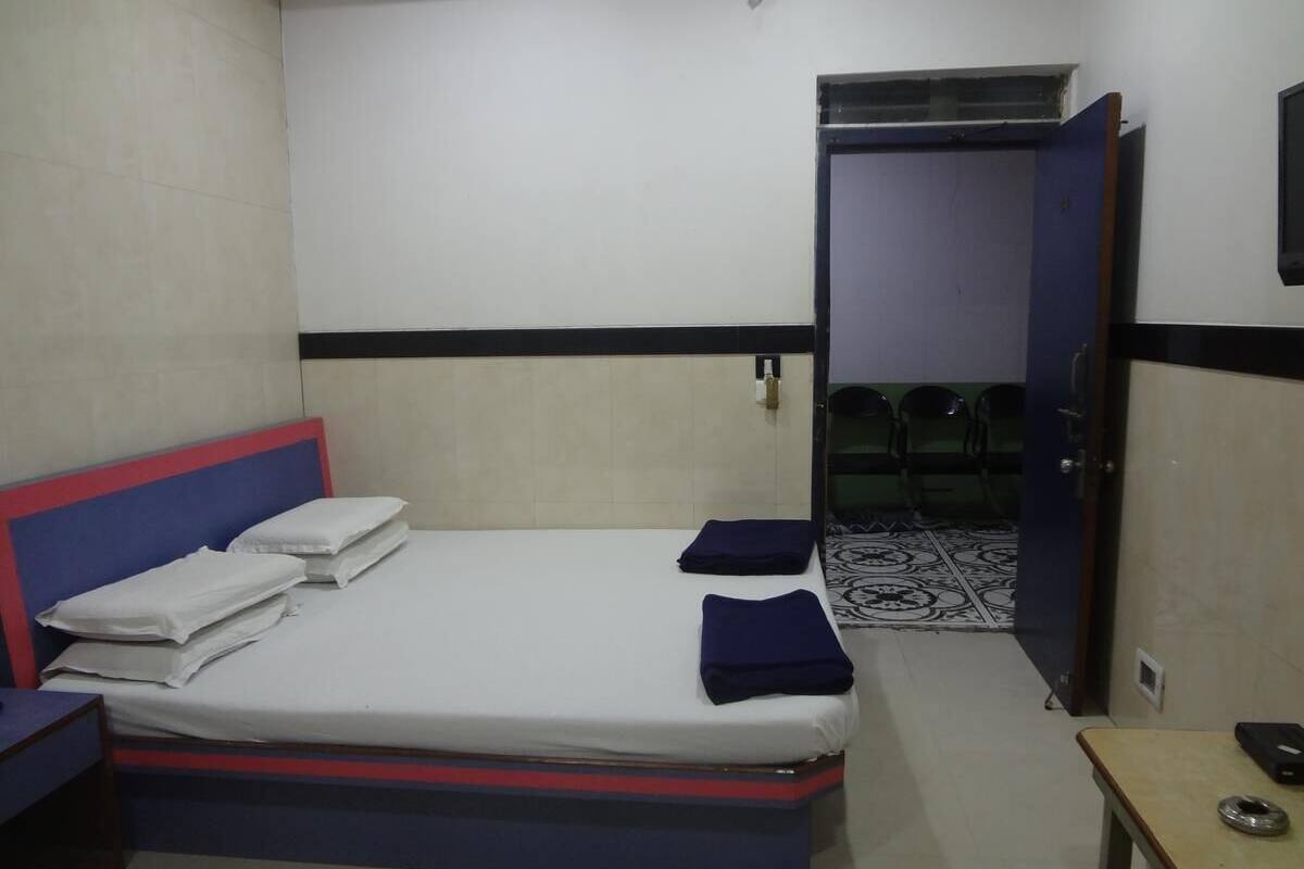 A hotel room with a bed, a bedside table, and a door leading to a hallway.