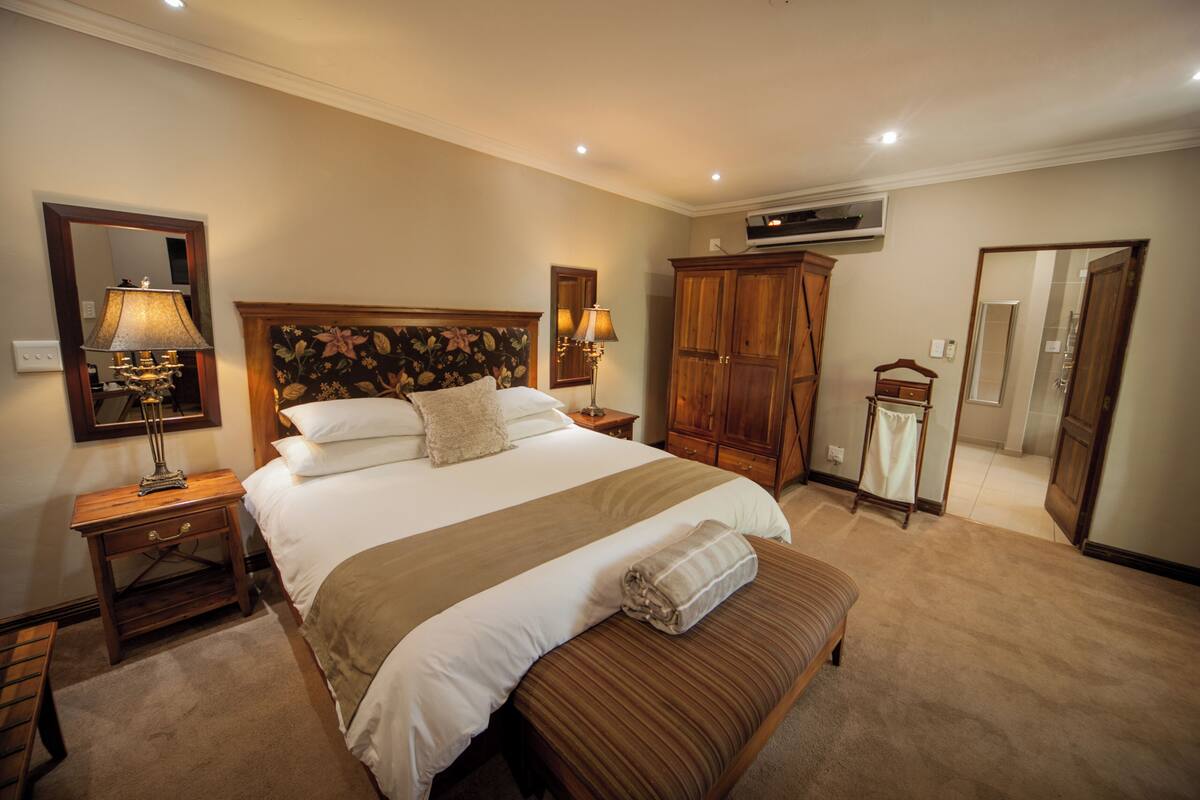 A hotel room with a large bed, wooden headboard, two bedside tables with lamps, a wardrobe, and a mirror.
