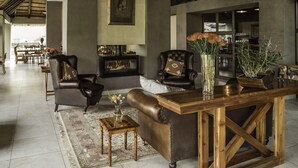 Een ruime lobby met leren banken, een houten salontafel en een open haard.