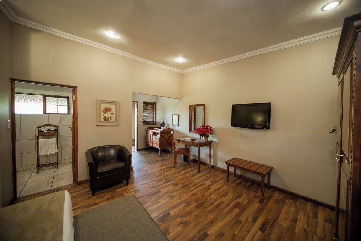 A spacious living room with hardwood flooring, a leather sofa, a wooden coffee table, and a television mounted on the wall.